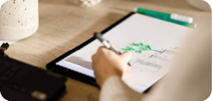An entrepreneur and designer is engrossed in sketching a new design for a concrete planter, surrounded by her work and previous creations, in the sunlit corner of her modern home.
