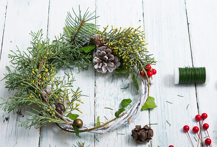 Couronne de Noël en sapinage avec feuillages variés, baies rouges et pommes de pin.