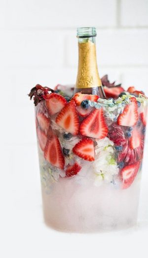 glaçons fleuris et fleurs en glaçons pour créer un seau à glace décoratif contenant fruits, fleurs et bouteille de champagne