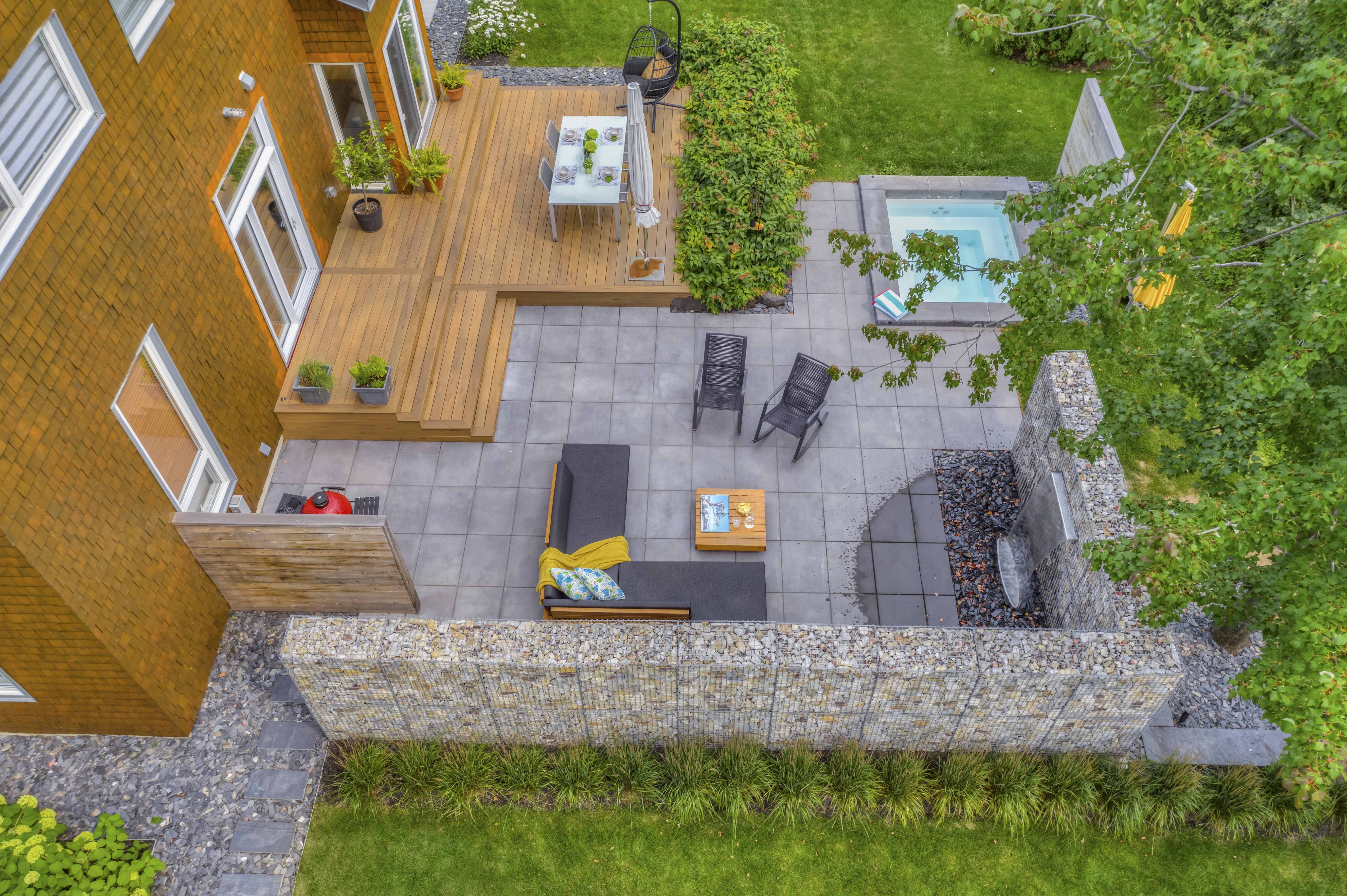 Vue aérienne d'une belle cour avec une terrasse en bois et dalles de béton cintrée d'un mur de gabion