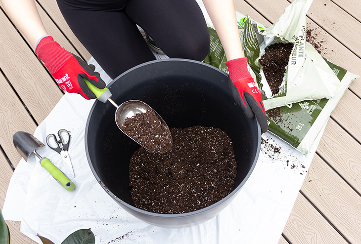 Une femme ajoute de la terre dans un pot de plante pour préparer ses pots pour la plantation de fleurs
