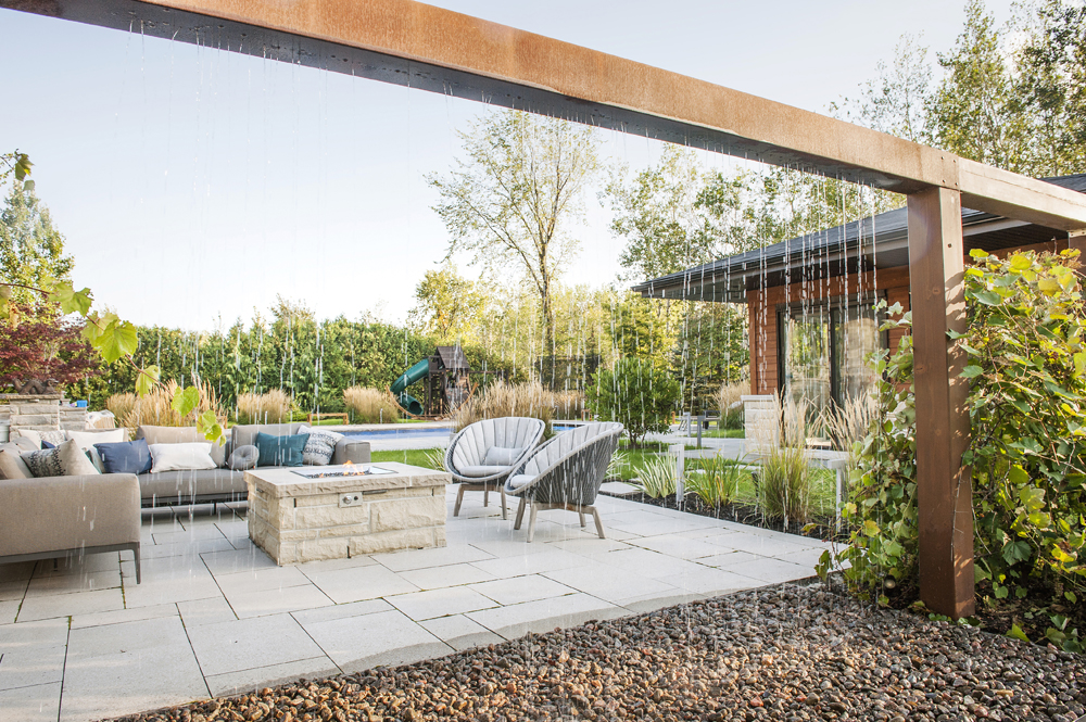 Espace de détente extérieur élégant avec canapés confortables sous un pavillon moderne doté d'un rideau de pluie, entouré de jardins luxuriants.