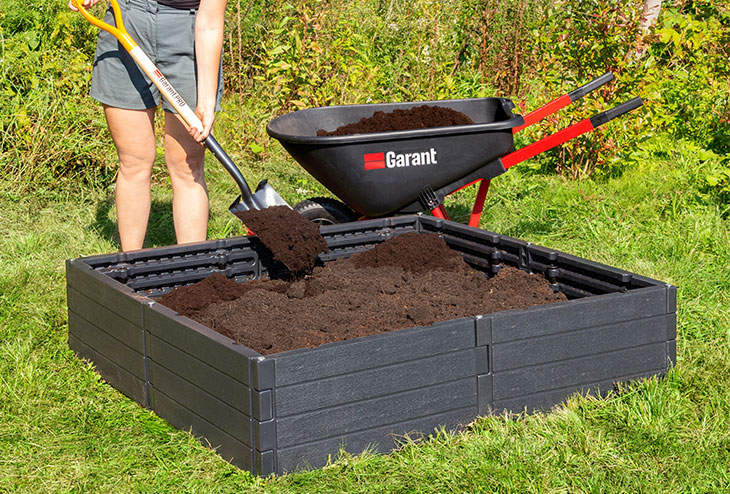 Une femme rempli son potager modulaire de terreau