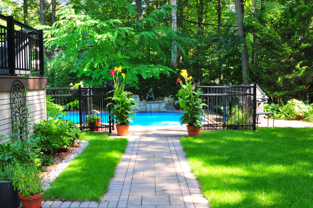 Allée en pavé menant à une piscine, bordée de fleurs et de verdure
