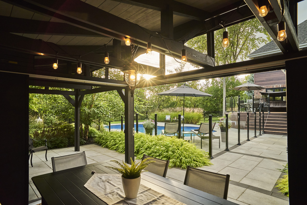 Vue du pavillon sur la piscine creusée, entourée de végétaux et clôturée de verre.