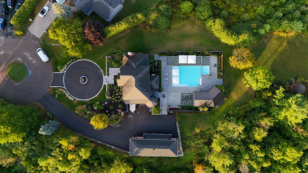 Vue aérienne d'une cour arrière aménagée avec piscine, pavillon, terrasses et plantations.